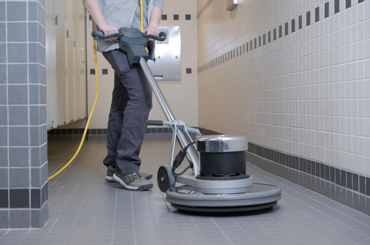 Cleaner scrubbing a tiled washroom floor with a rotary machine in Birmingham